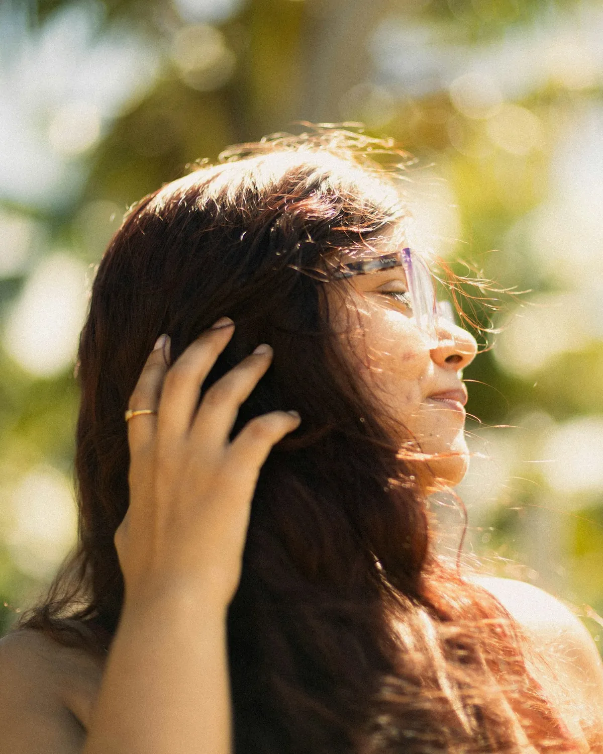 A woman with long hair gently running her hand through it in warm sunlight